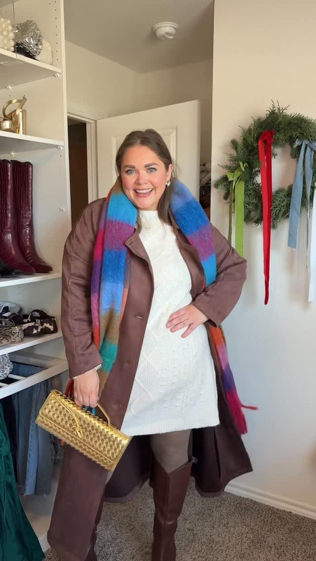 Smiling woman wearing a white sweater dress, brown coat, and colorful plaid scarf.