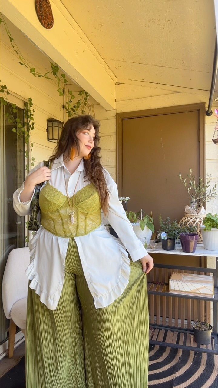 A woman posing in a green corset top and matching wide-leg pleated trousers on a porch.