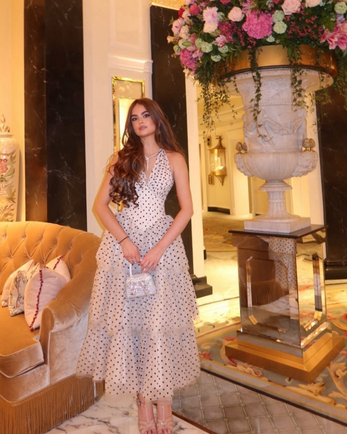 Woman in a polka dot midi dress posing with strappy high heels in an elegant room.