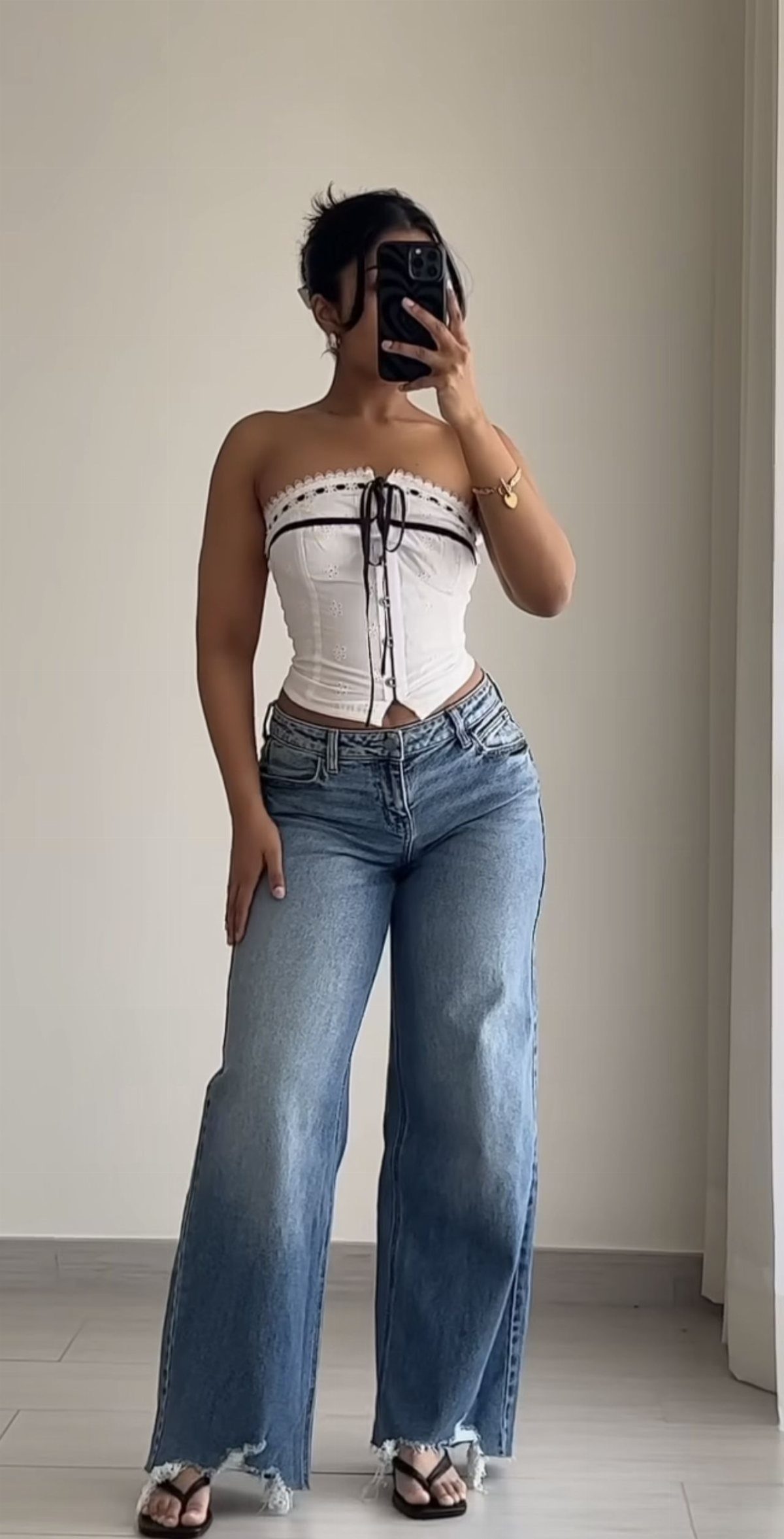 Woman in a white corset top and wide-leg blue jeans taking a mirror selfie.