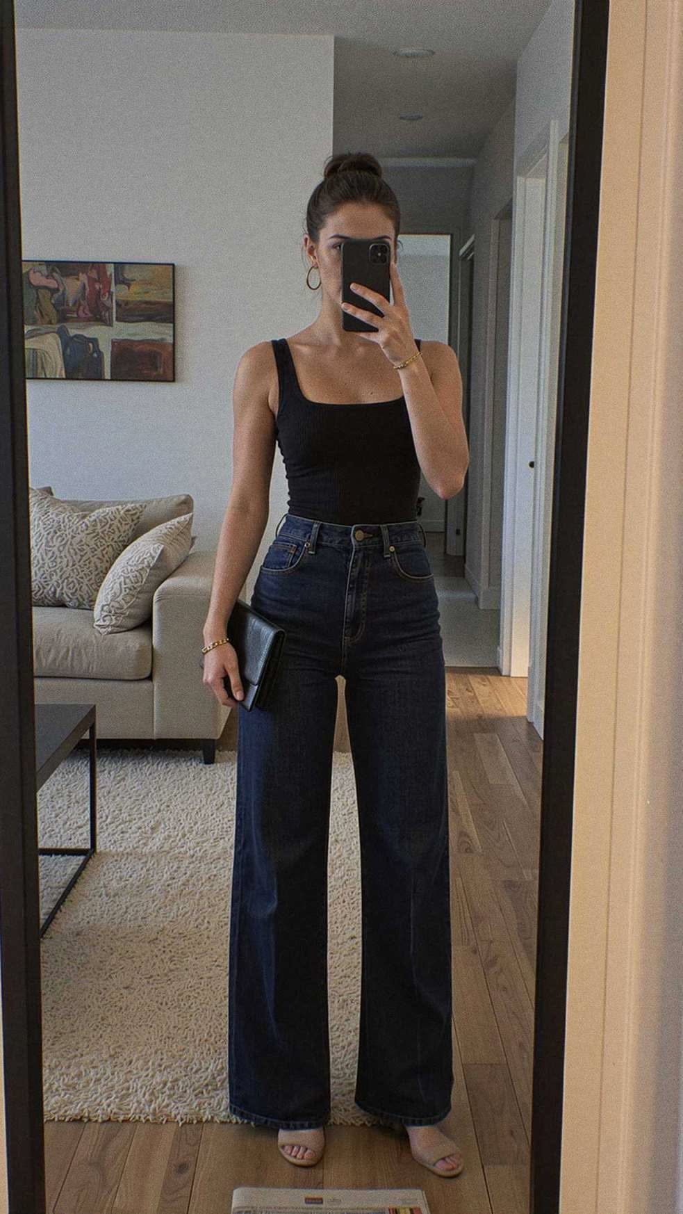 A woman wearing a black tank top and dark blue high-waisted wide-leg jeans.