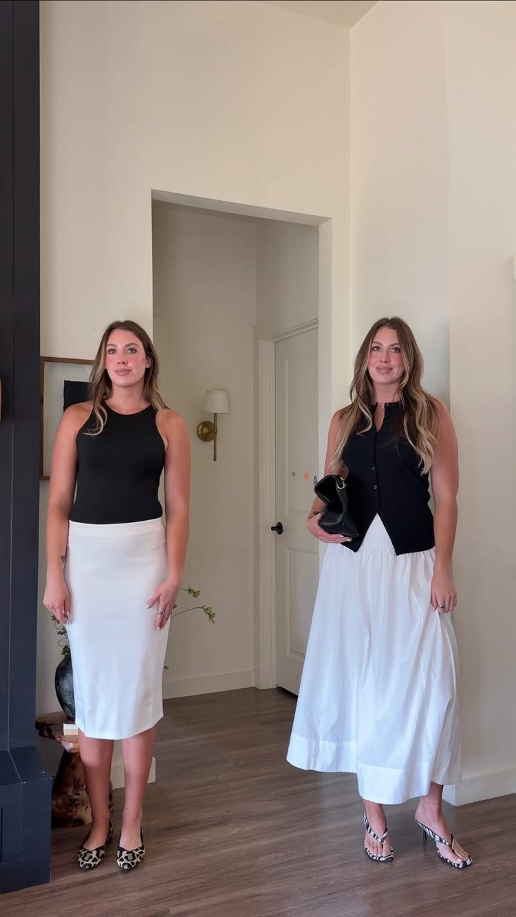 Two women posing in black tops and white skirts in a bright room.