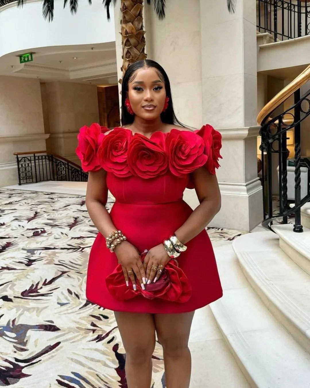 Woman wearing a red mini dress with large rose shoulder embellishments in a hotel lobby.