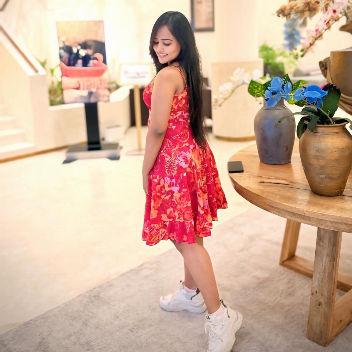 A woman in a red floral mini dress and white sneakers posing indoors.