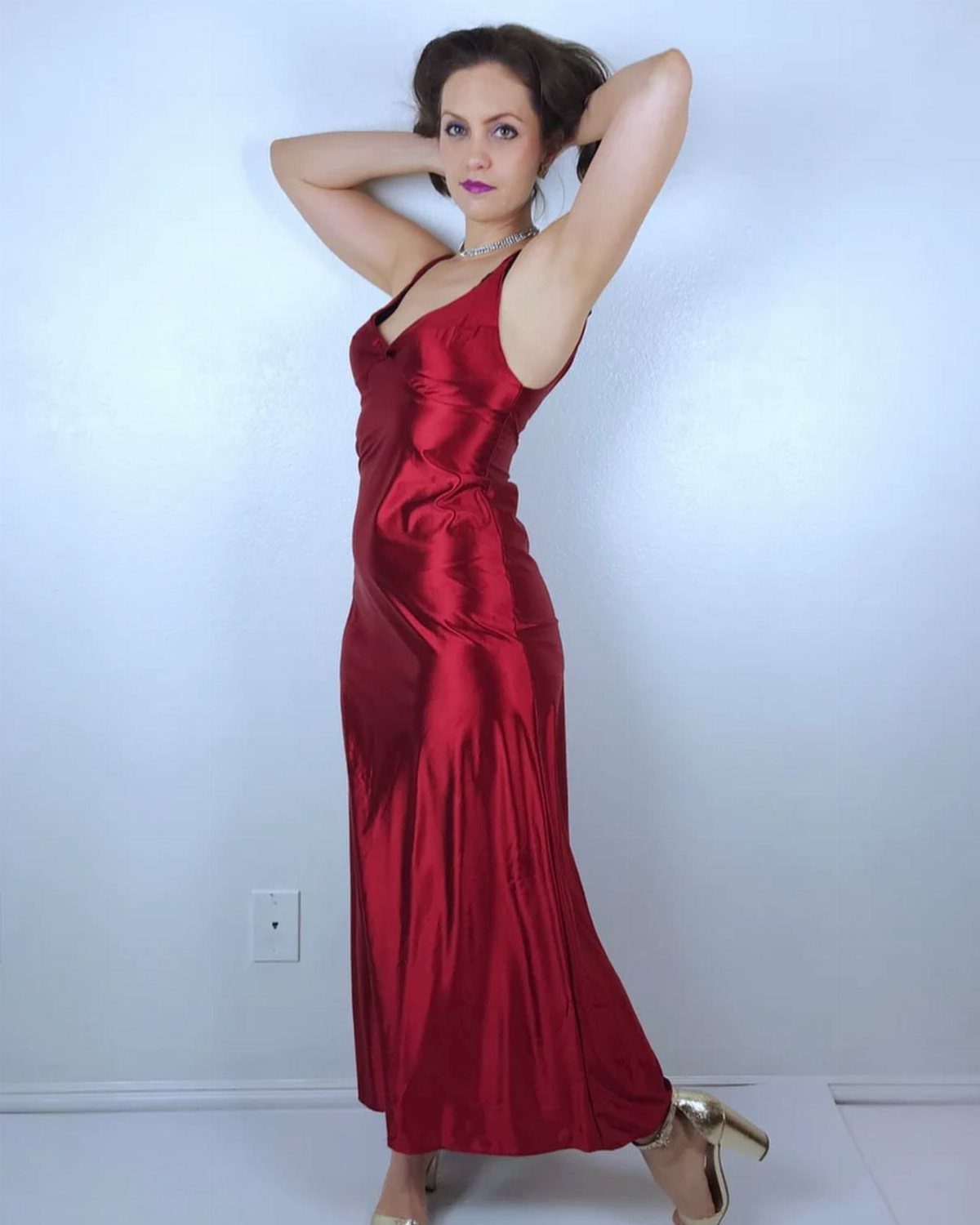 Woman posing in a long scarlet red satin slip dress and gold heels.