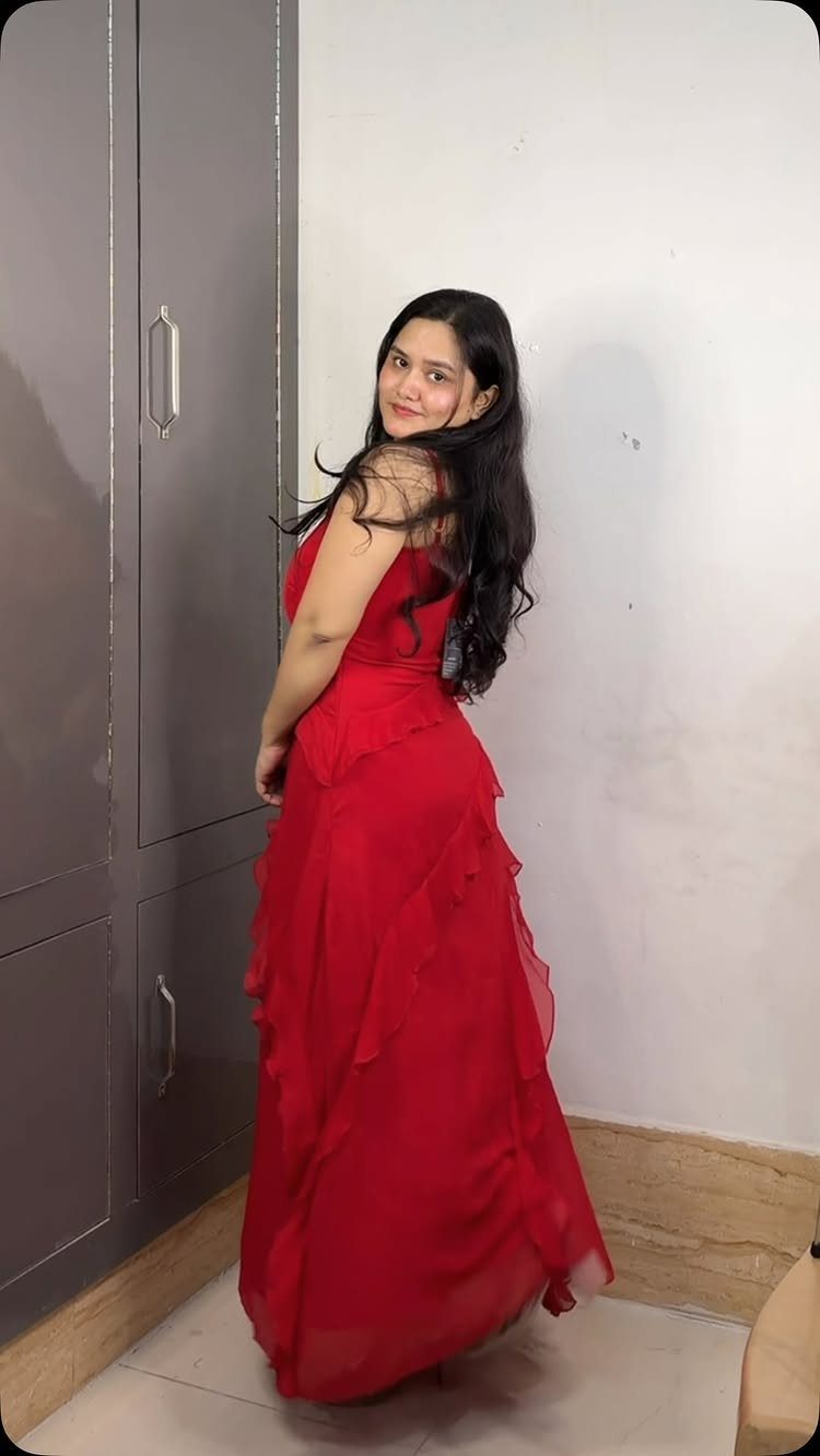 A woman posing in a long red dress with ruffles along the skirt.