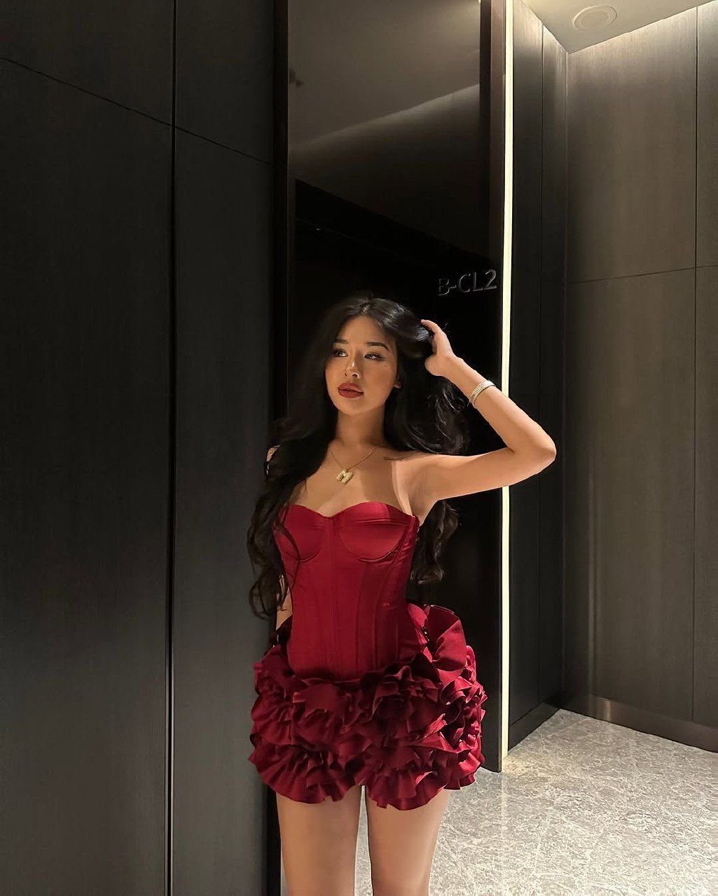 A woman posing in a red satin corset mini dress with ruffles.
