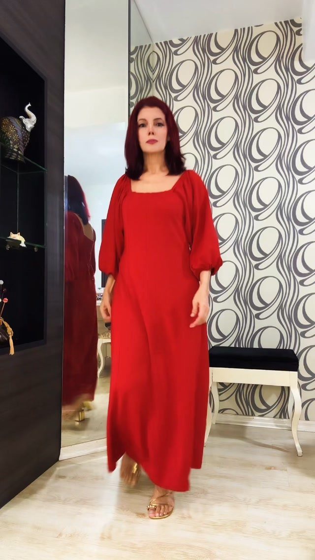 A woman with red hair wearing a long, flowing red dress standing in a room.