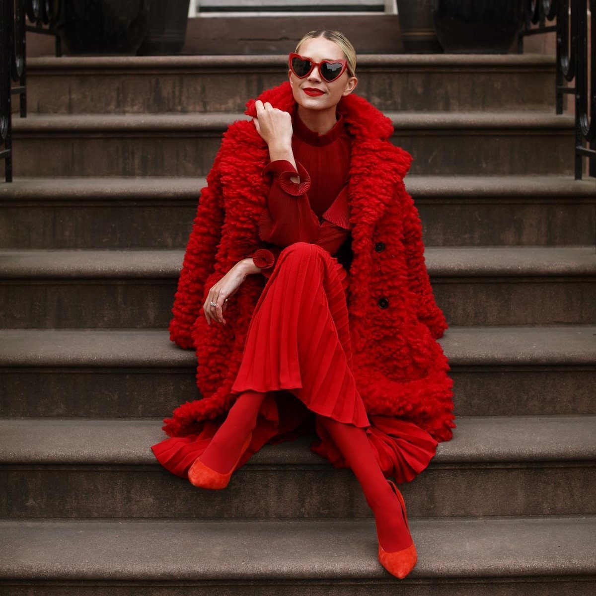 Woman sitting on stone stairs wearing a full monochromatic red outfit including a textured coat and pleated dress.