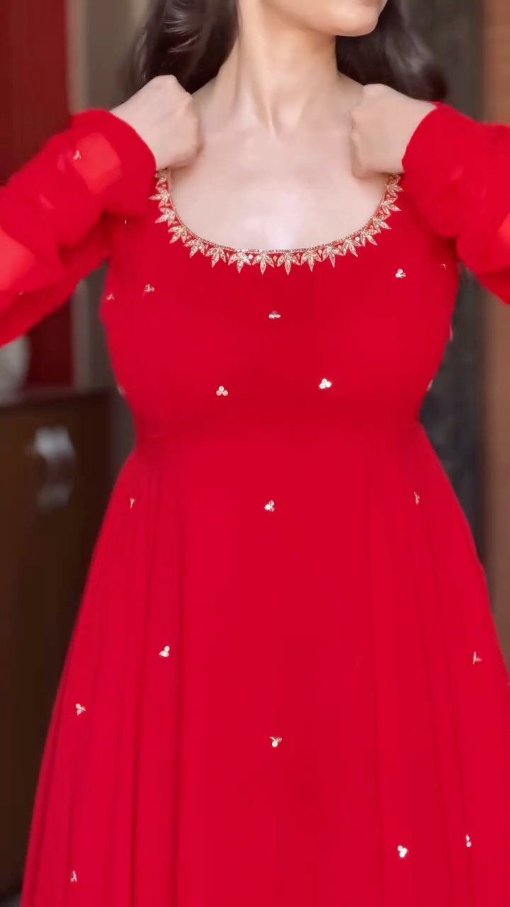 A woman wearing a red dress with gold embroidery around the scoop neckline.