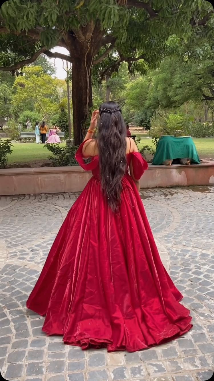 Woman in a voluminous red floor-length gown standing in a garden setting facing away.