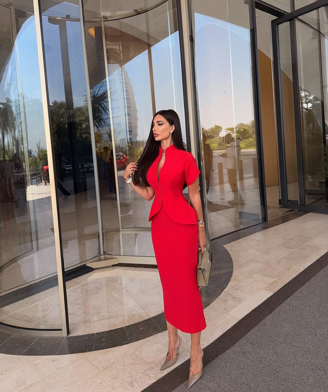 A woman in a tailored red peplum dress standing in front of a glass building.