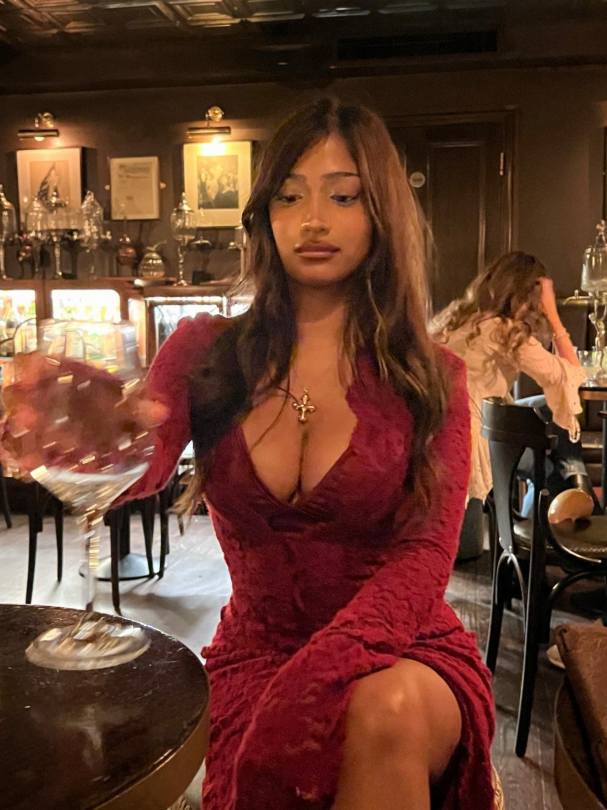 A woman in a deep red lace dress sitting at a table in a dimly lit lounge.