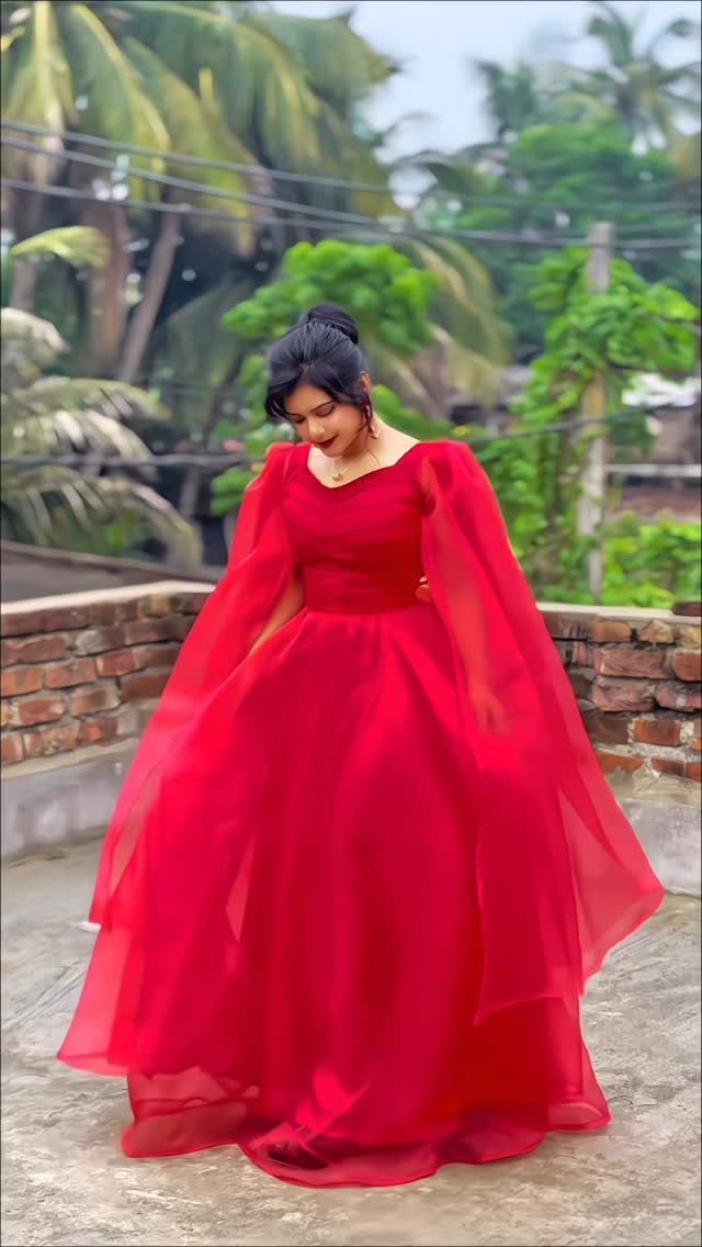 A woman posing in a voluminous red organza gown with flowing sheer sleeves outdoors.