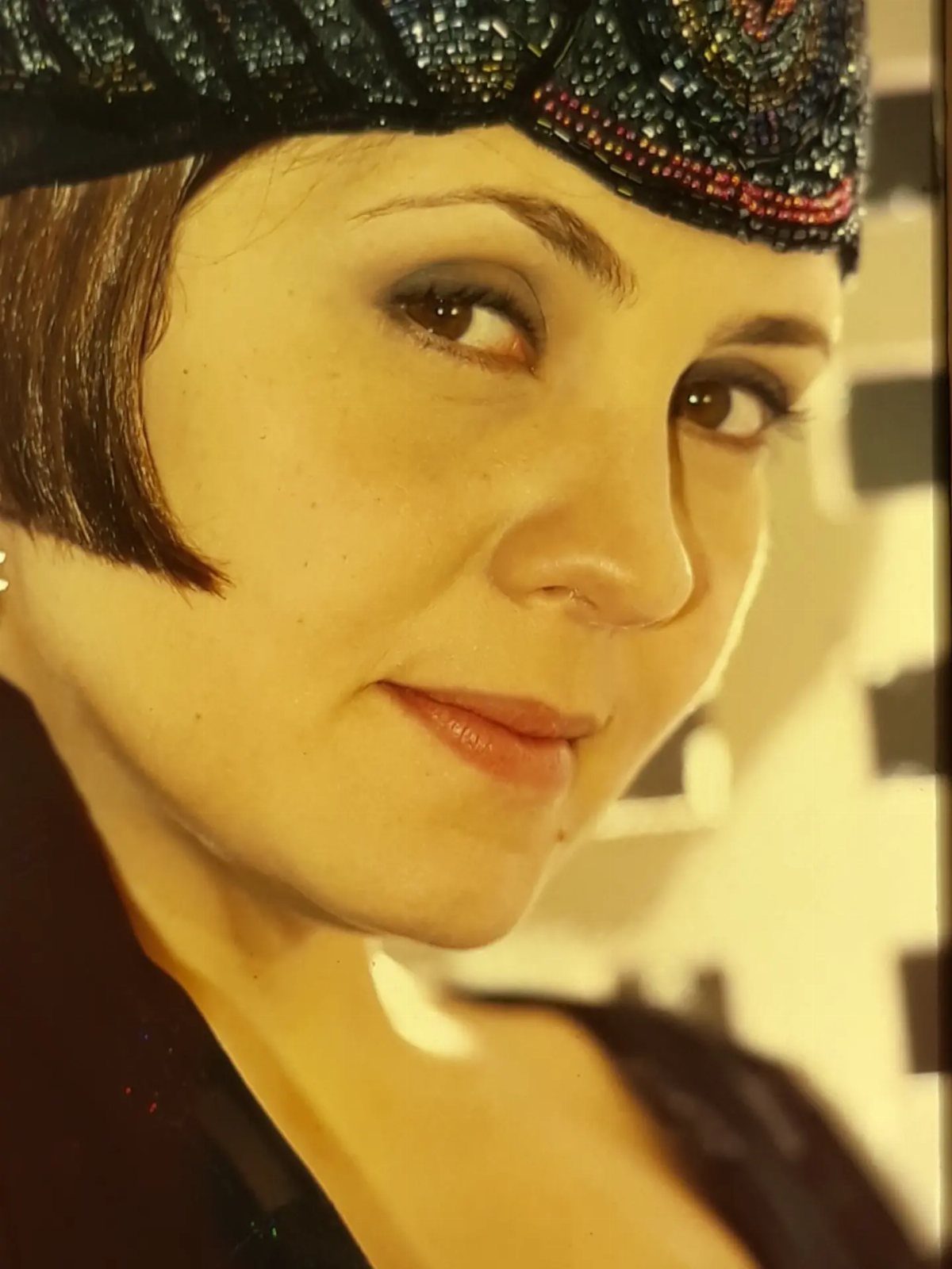 A woman wearing a dark, intricately beaded headband with colorful patterns and short dark hair.
