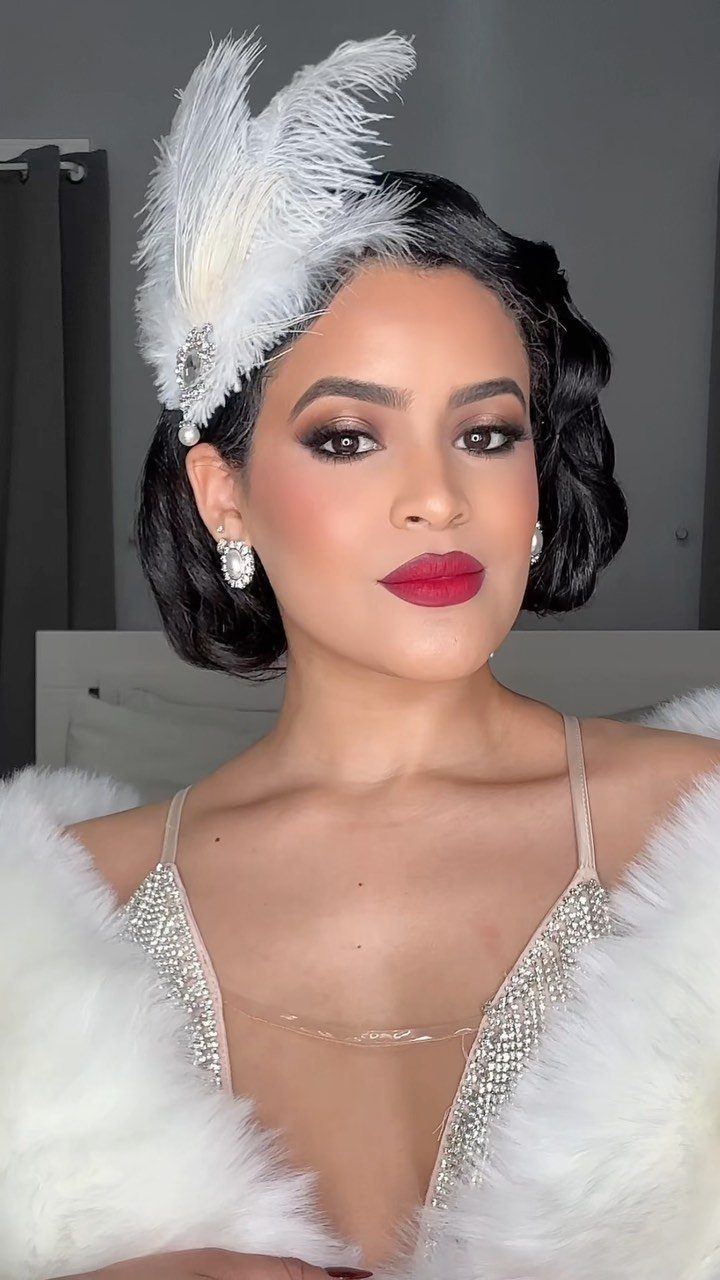 Woman with dark finger waves, smoky eye makeup, bold red lips, and a white feathered headband.