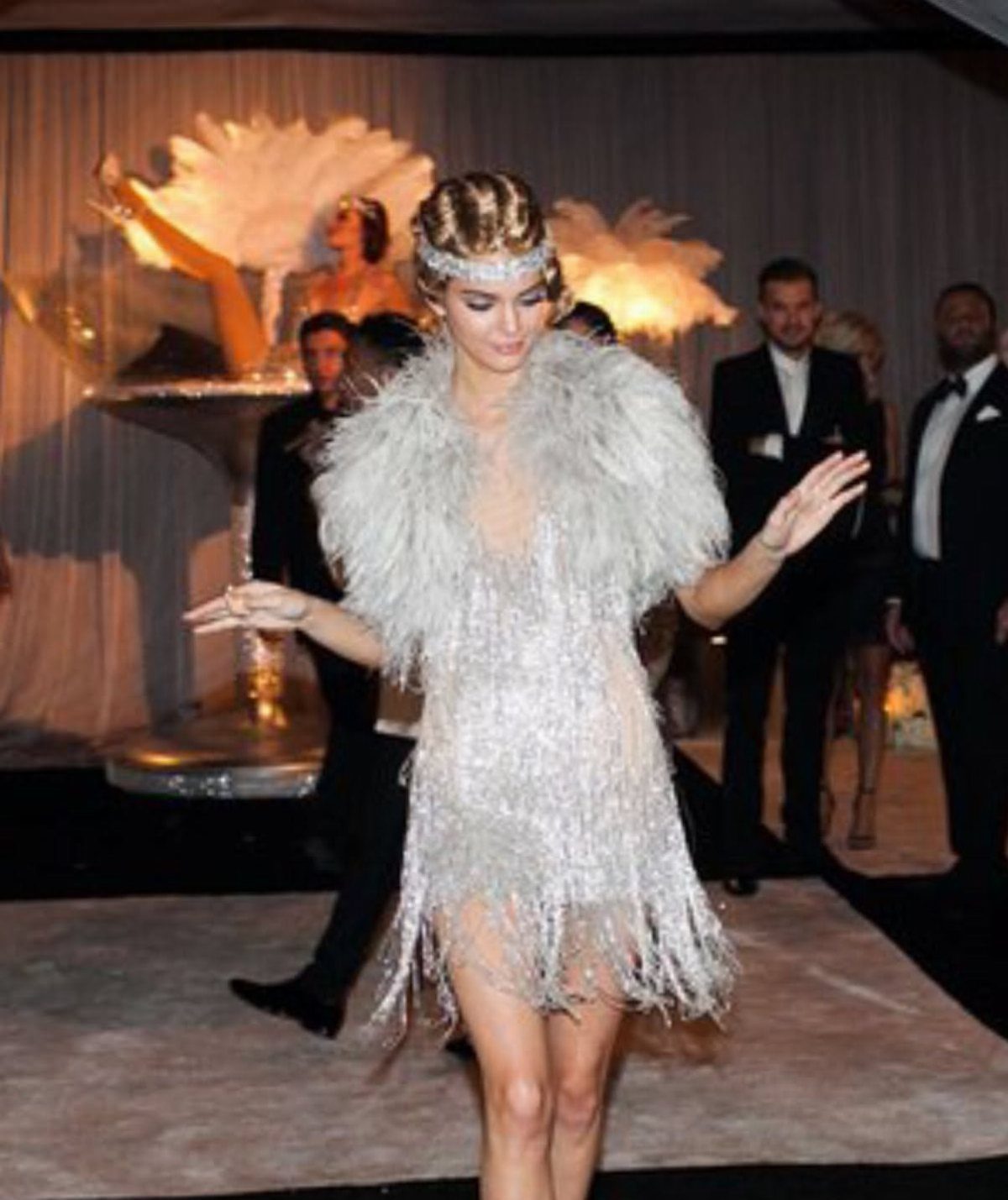 Woman wearing a silver fringe dress and feathered stole at a vintage themed party.