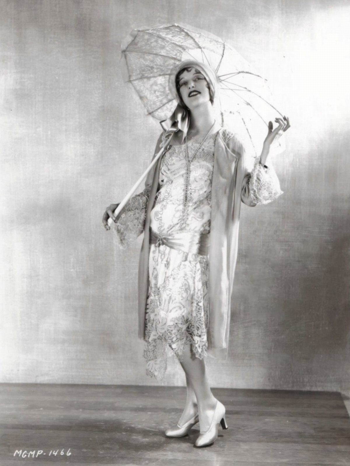 A woman in a vintage lace dress and cloche hat holding a decorative parasol.