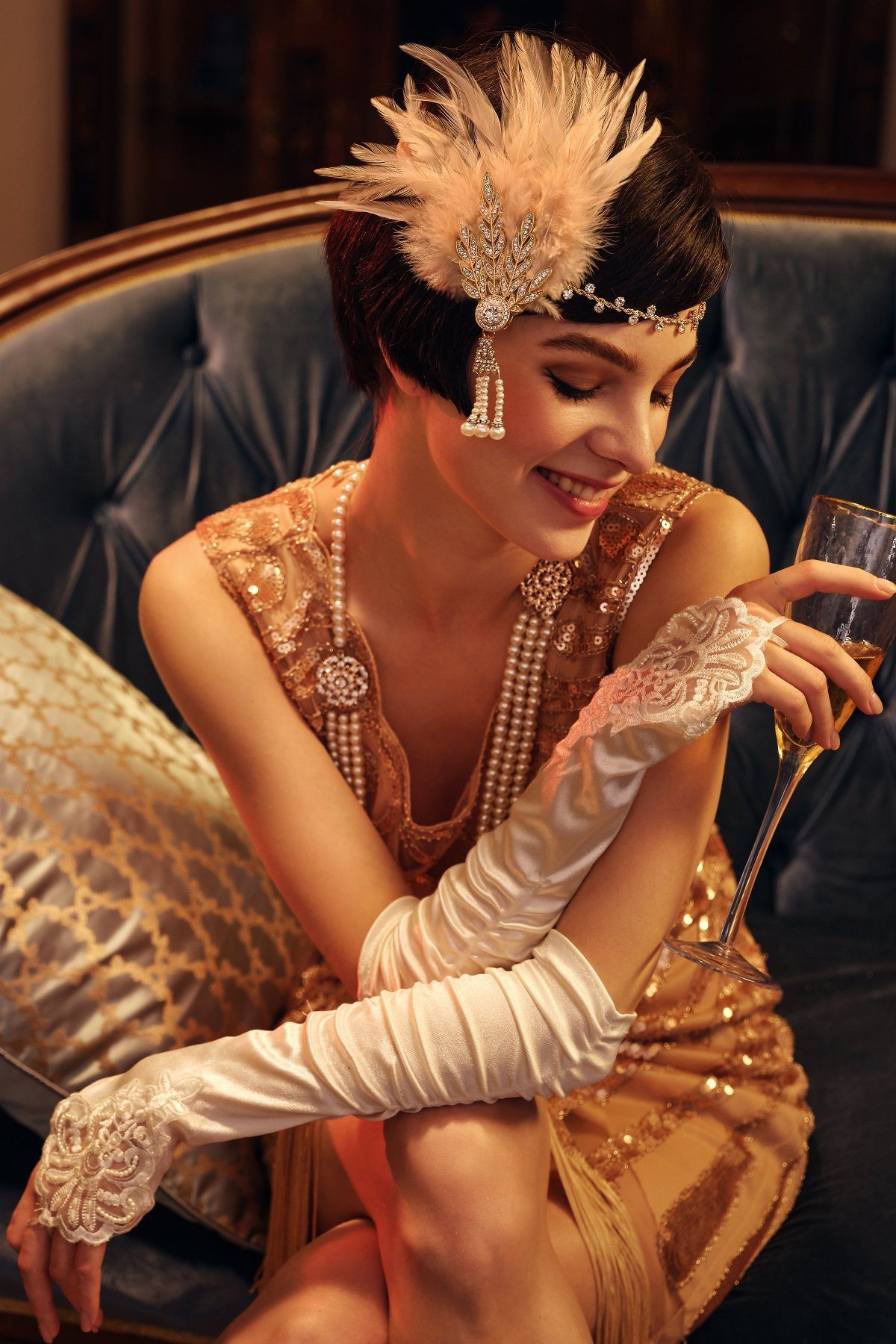 Woman in flapper attire wearing long white satin gloves and pearl necklaces on a blue sofa.
