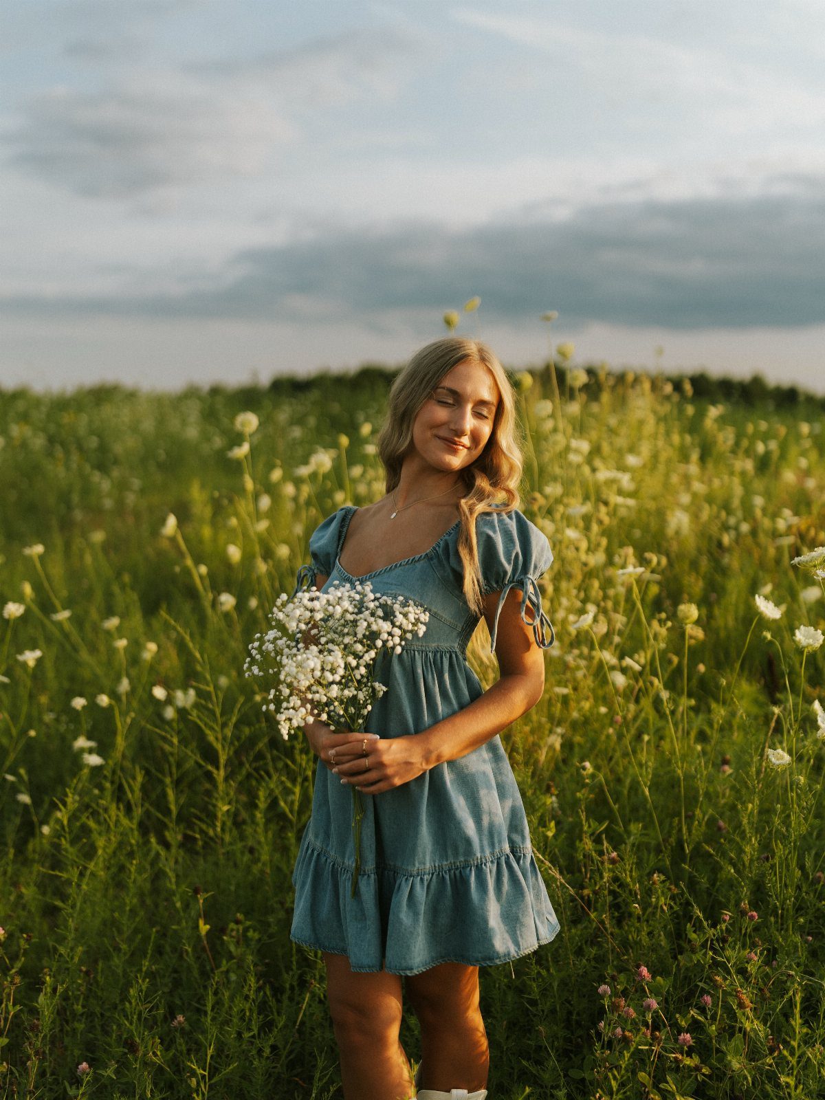 Young woman in a blue puff-sleeve dress holding white flowers in a grassy field.
