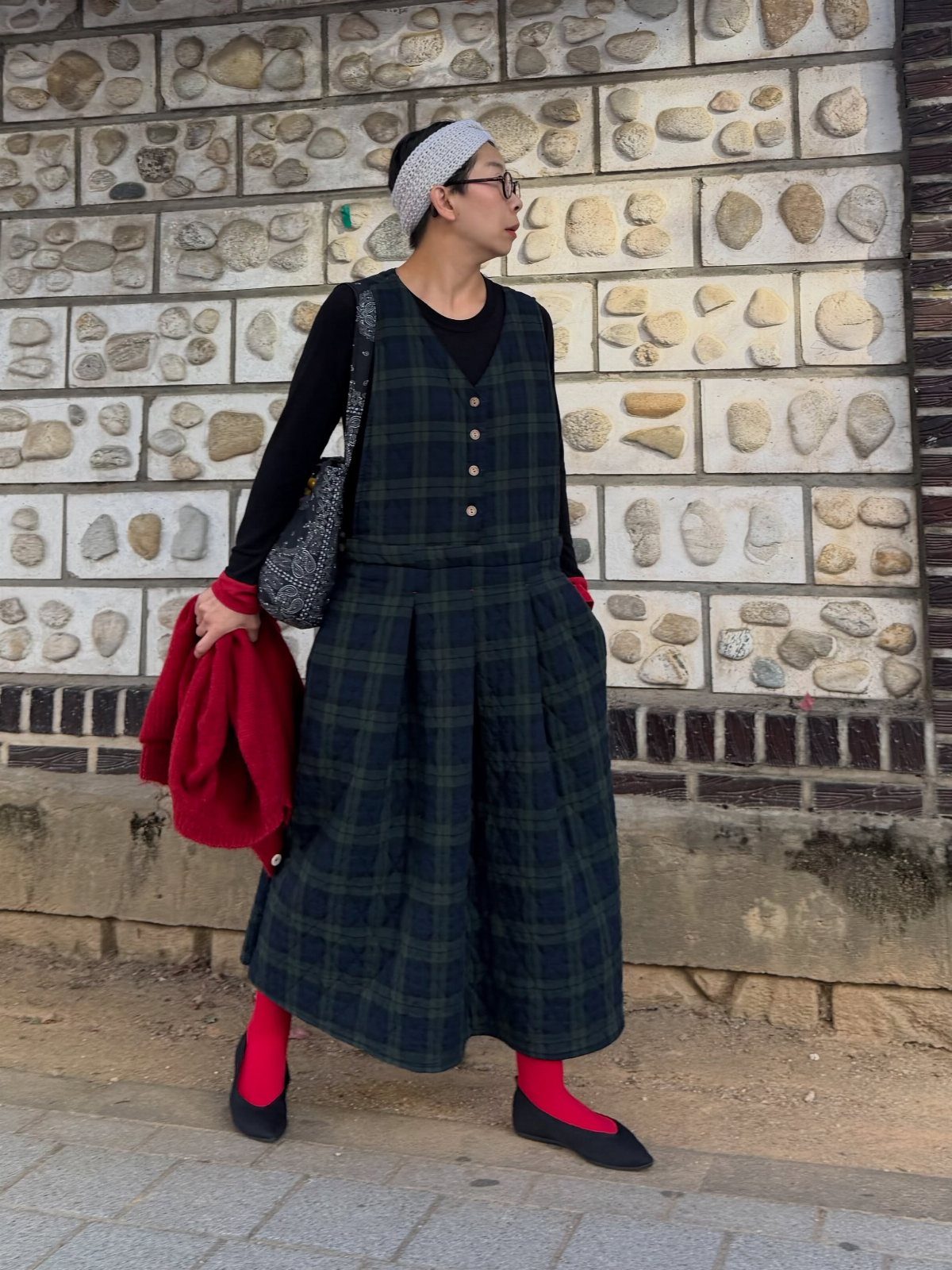 A person wearing a dark green checkered vest and matching wide-leg trousers with red socks.