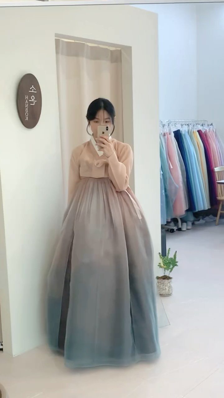 Woman in a modern hanbok posing for a mirror selfie in a clothing boutique.
