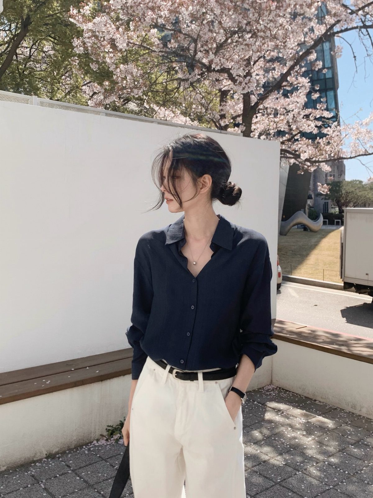 A woman wearing a navy shirt and cream trousers standing near blooming cherry blossom trees.