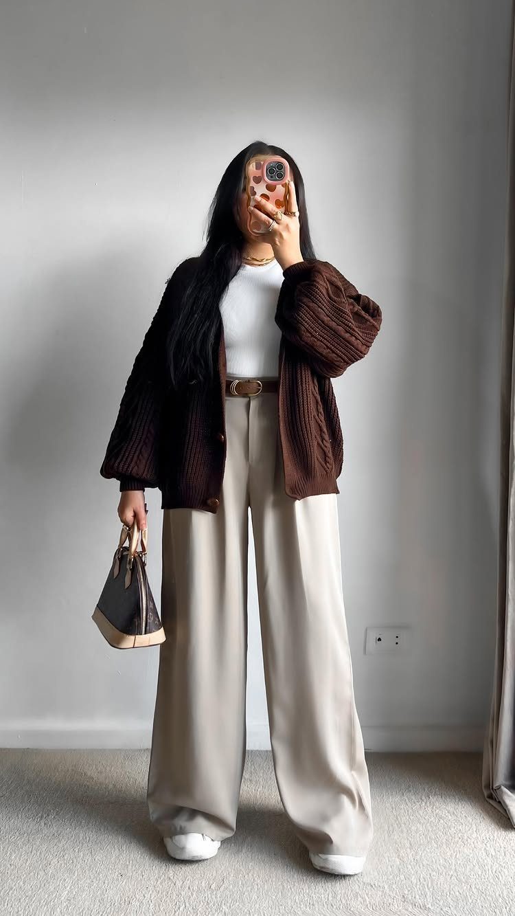 A person posing in a brown ribbed cardigan, white top, and beige wide-leg trousers.