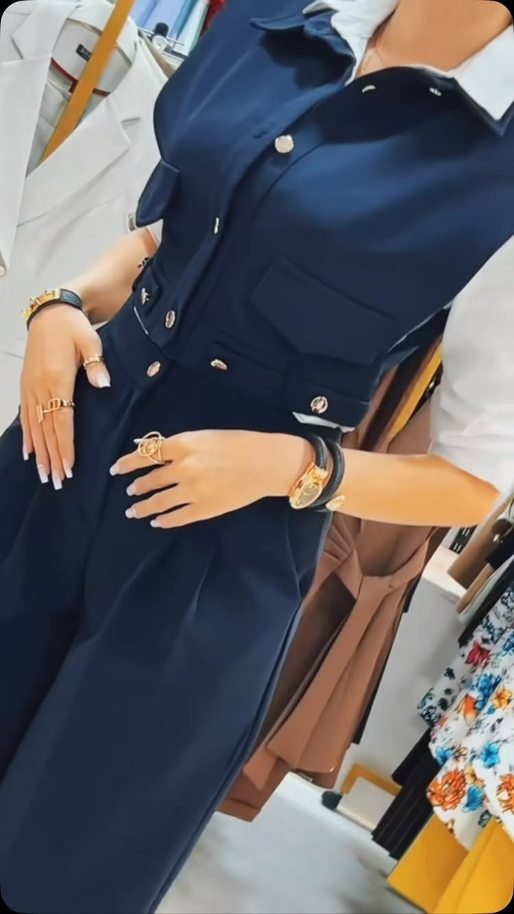 A person wearing a navy blue vest and matching trousers with gold jewelry accessories.