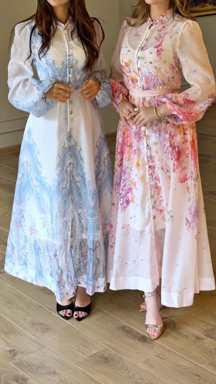 Two women wearing long floral and watercolor patterned maxi dresses standing on a wooden floor.