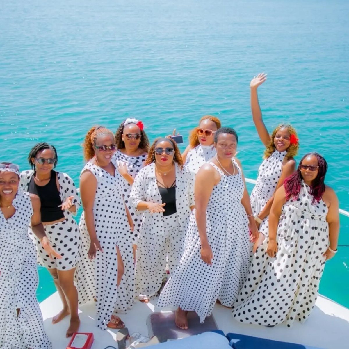 Group of women wearing matching white and black polka dot summer dresses on a boat.