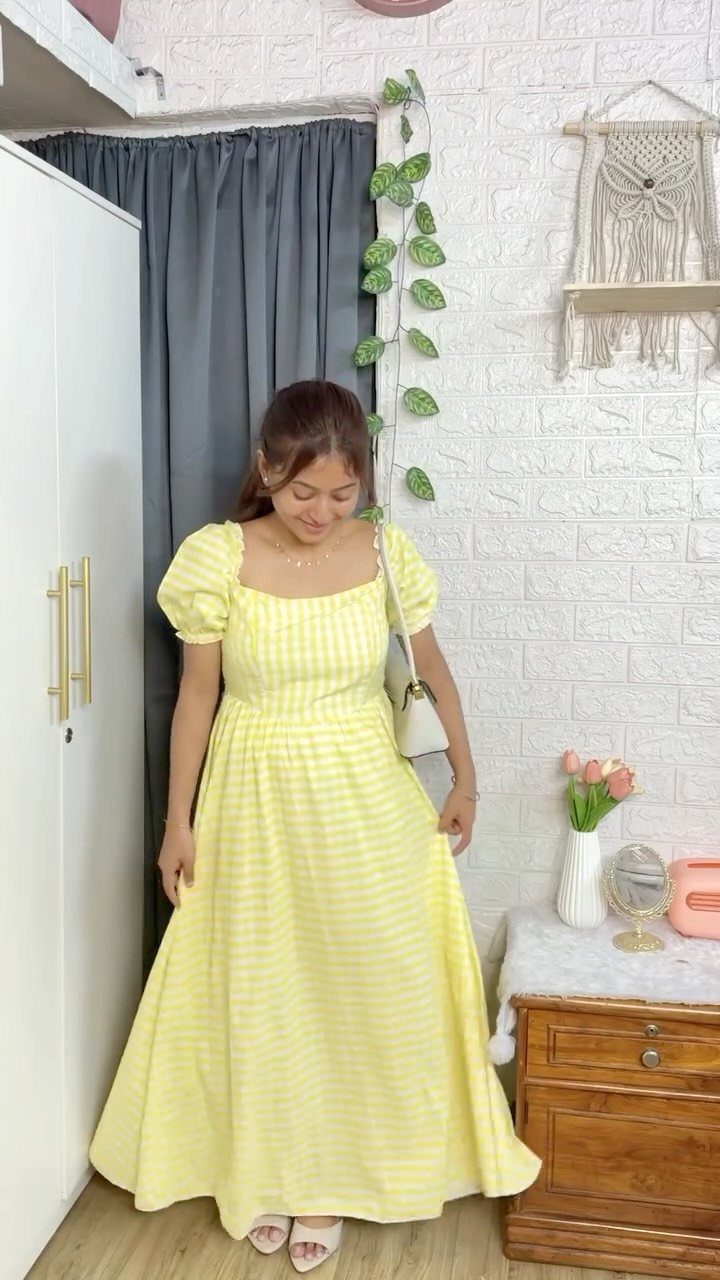 A smiling woman wearing a long yellow and white striped puff-sleeve summer dress.