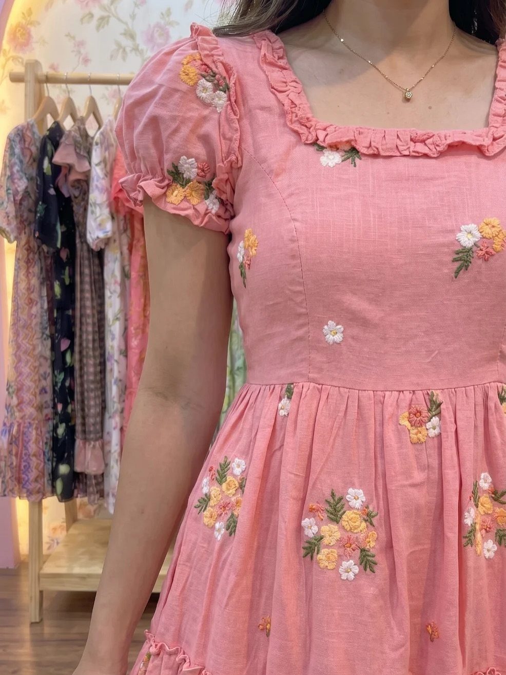 A person wearing a pink floral embroidered linen dress with ruffled sleeves.