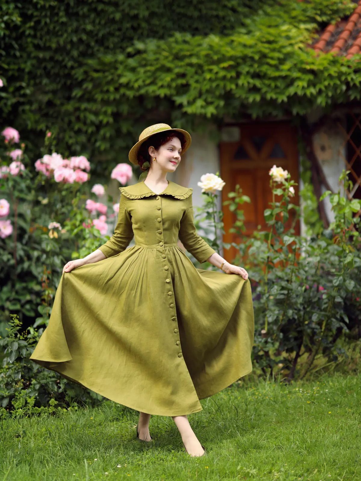 A woman in an olive green linen midi dress posing in a blooming rose garden.