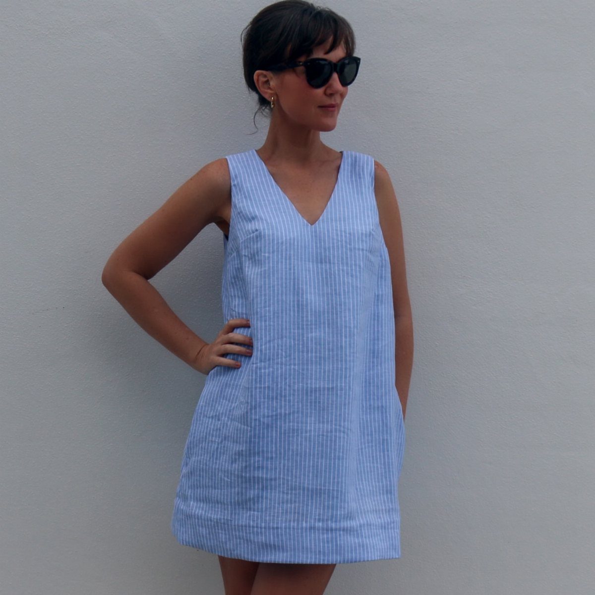 Woman in a blue striped sleeveless shift dress posing against a grey wall.