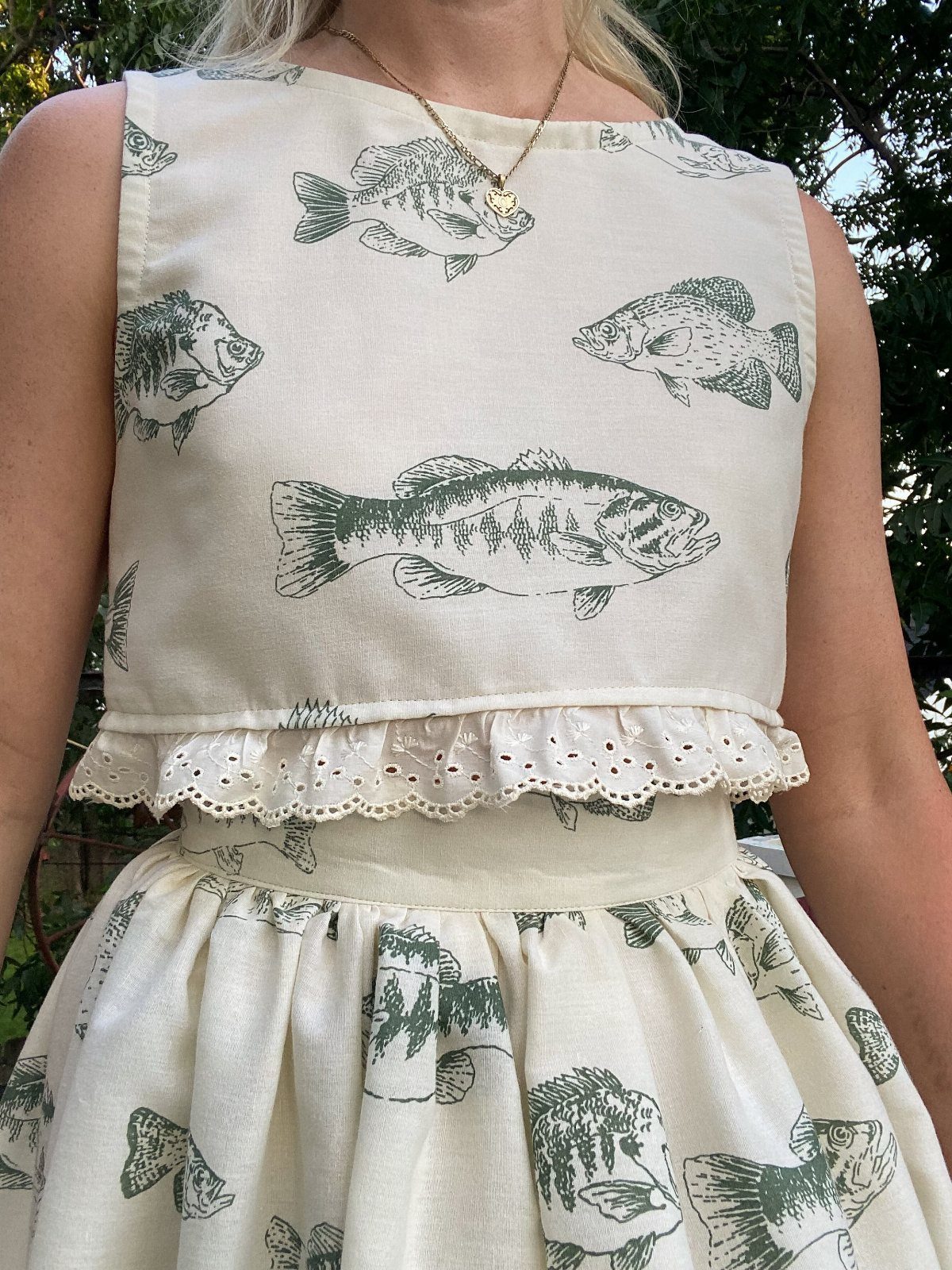 A person wearing a cream linen dress with a green fish print pattern and ruffled details.
