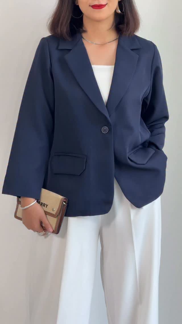 Woman wearing a navy blue blazer, white top, and white wide-leg trousers holding a clutch.