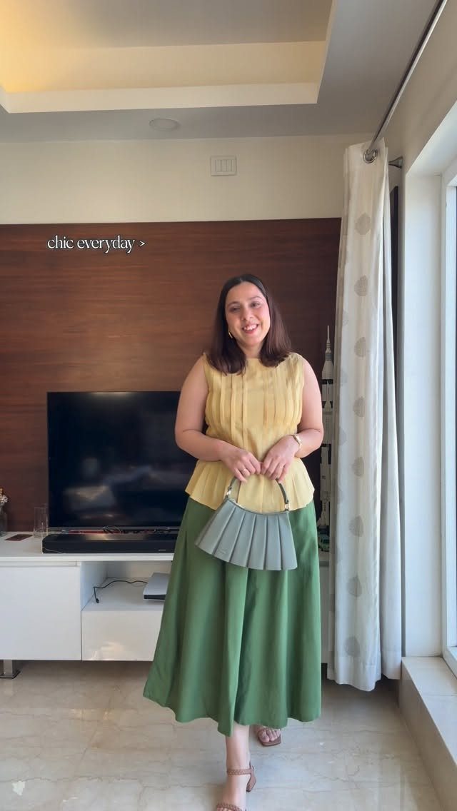 A woman posing in a yellow sleeveless top and a long green midi skirt.