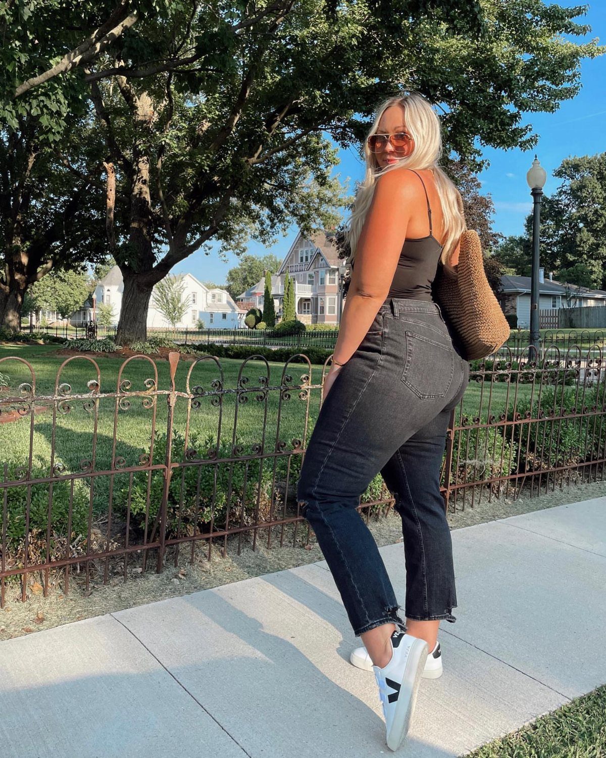 A woman wearing a black bodysuit and black denim jeans posing on a sunny sidewalk.