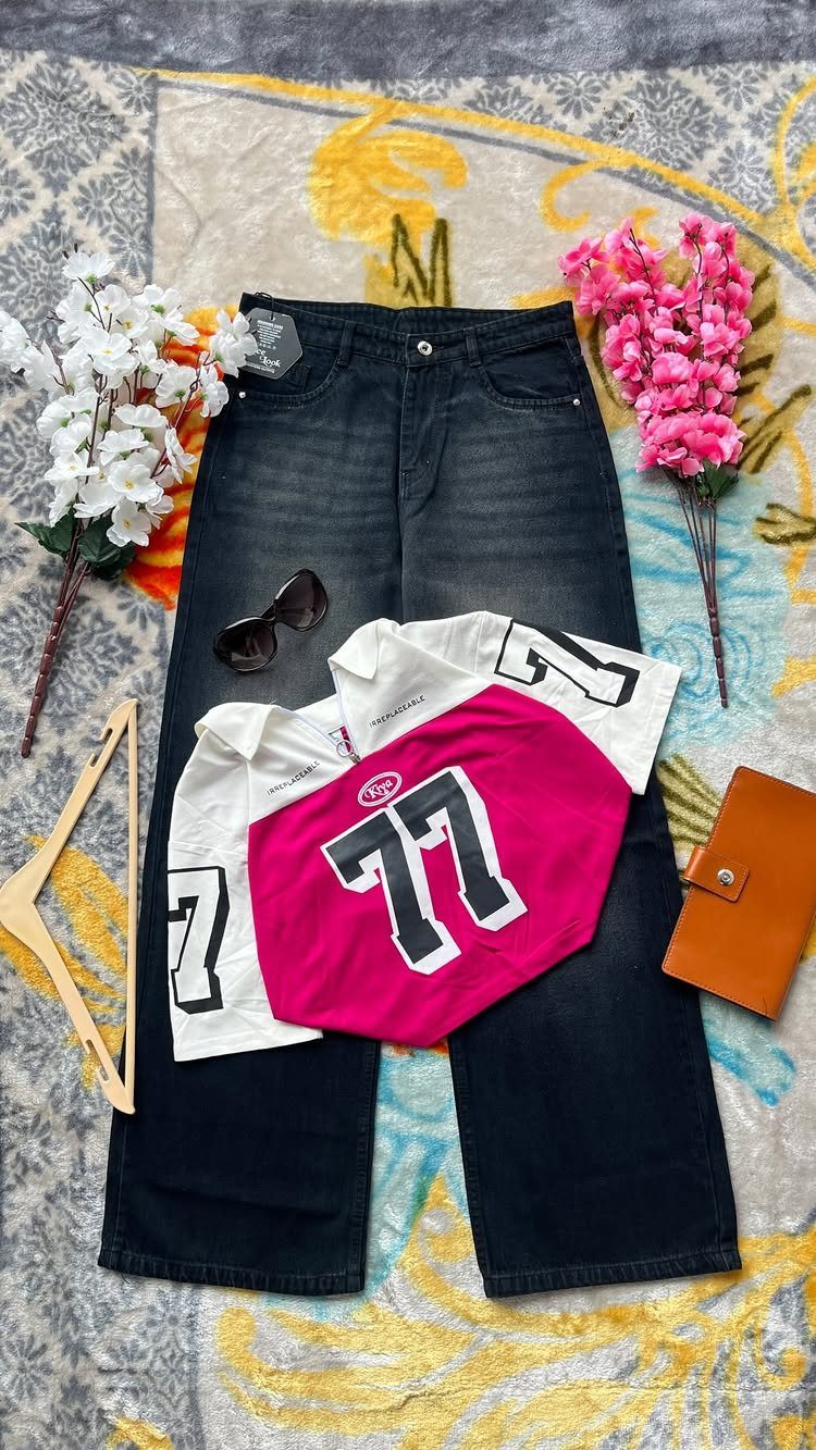 A pink cropped jersey top with number 77 laid over dark denim jeans with accessories.