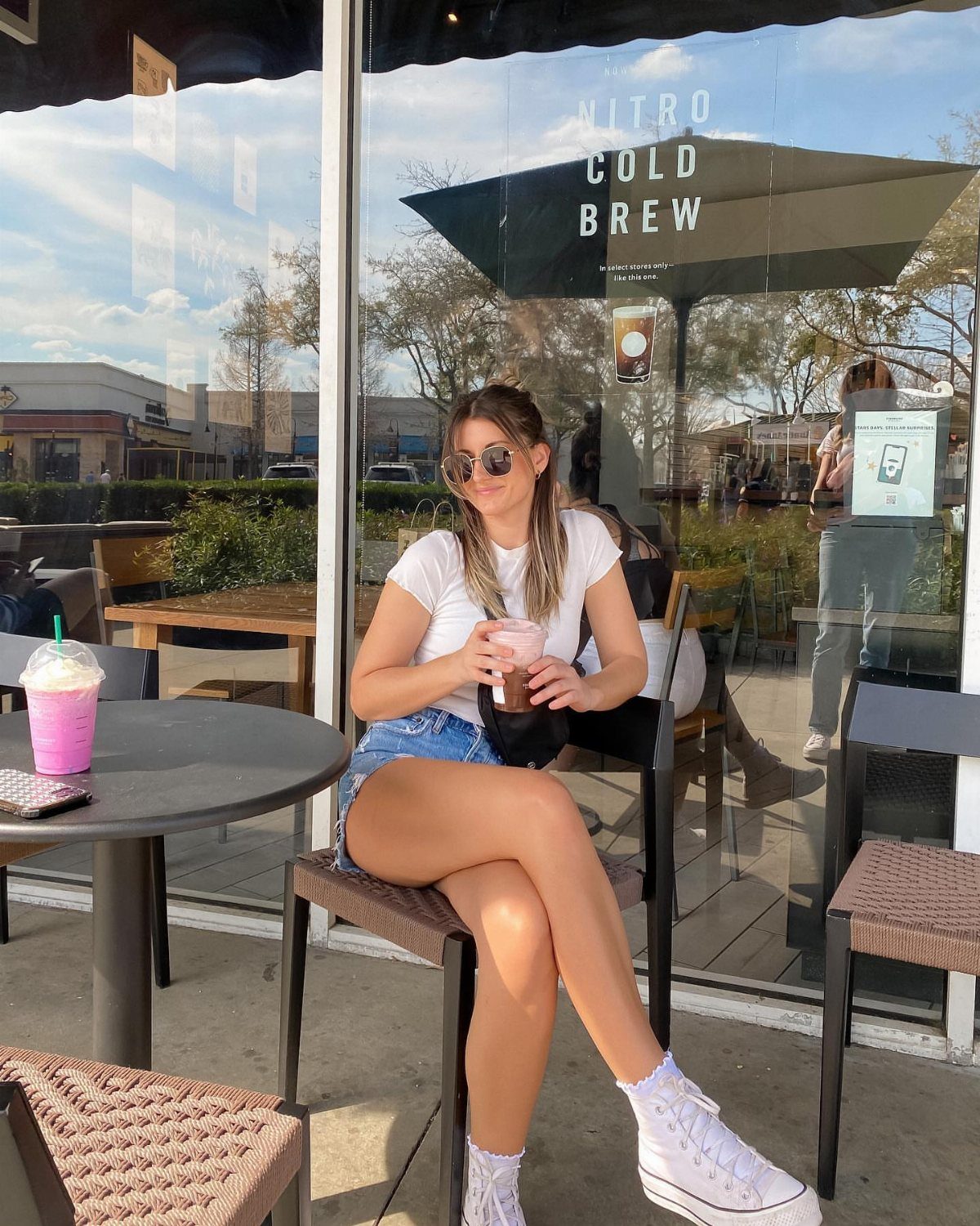 A woman in a white t-shirt and denim shorts sitting at an outdoor cafe table.