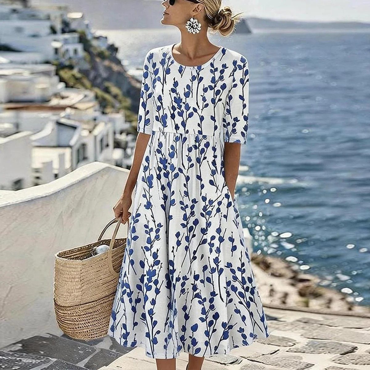 Woman in a blue and white floral A-line dress standing by the sea with a straw basket.