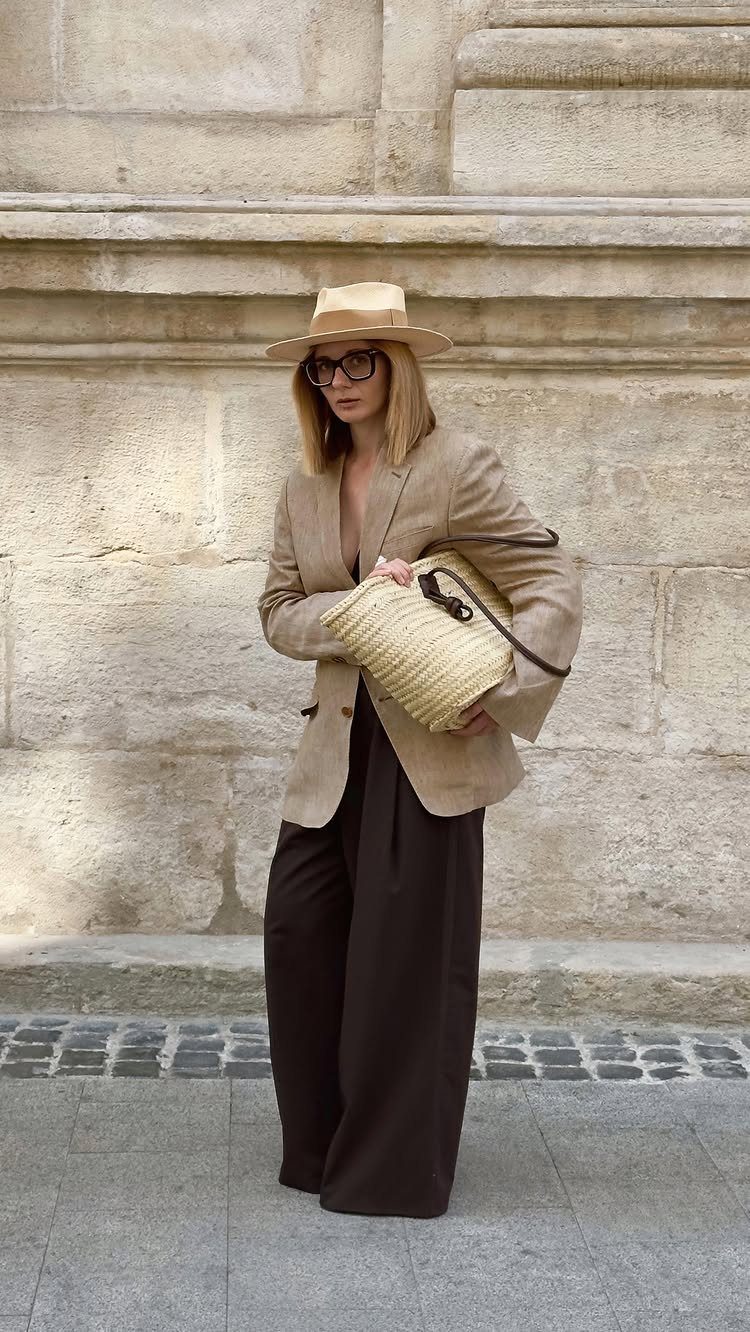 A woman in a beige blazer and dark trousers wearing a tan fedora hat.