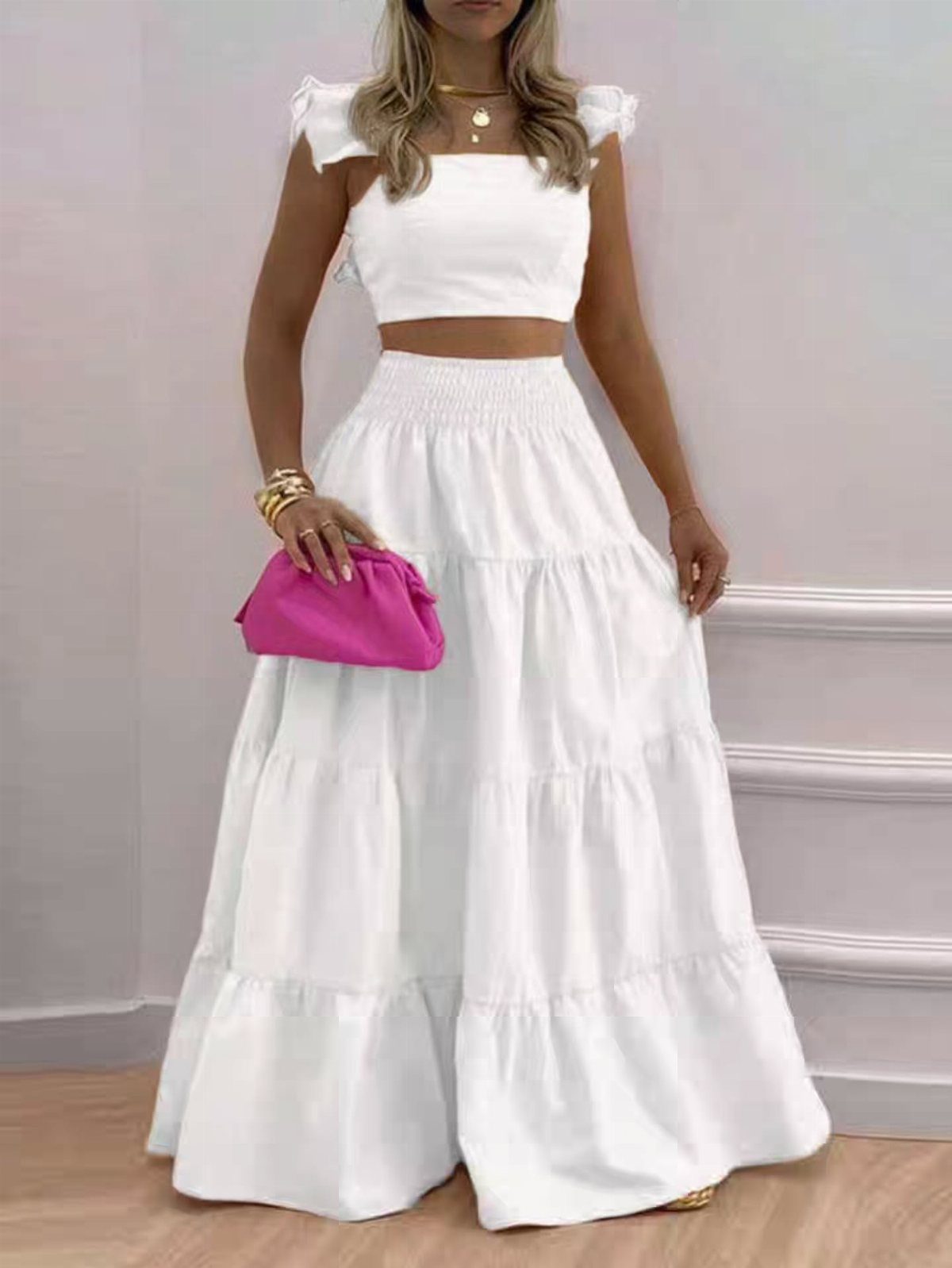 Woman wearing a white tiered maxi skirt and matching cropped top holding a pink clutch.