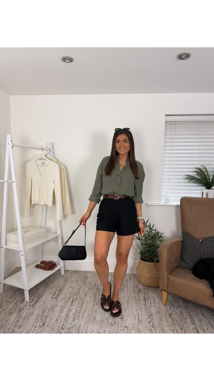 A woman posing in a green shirt and black high waisted shorts with a brown belt.