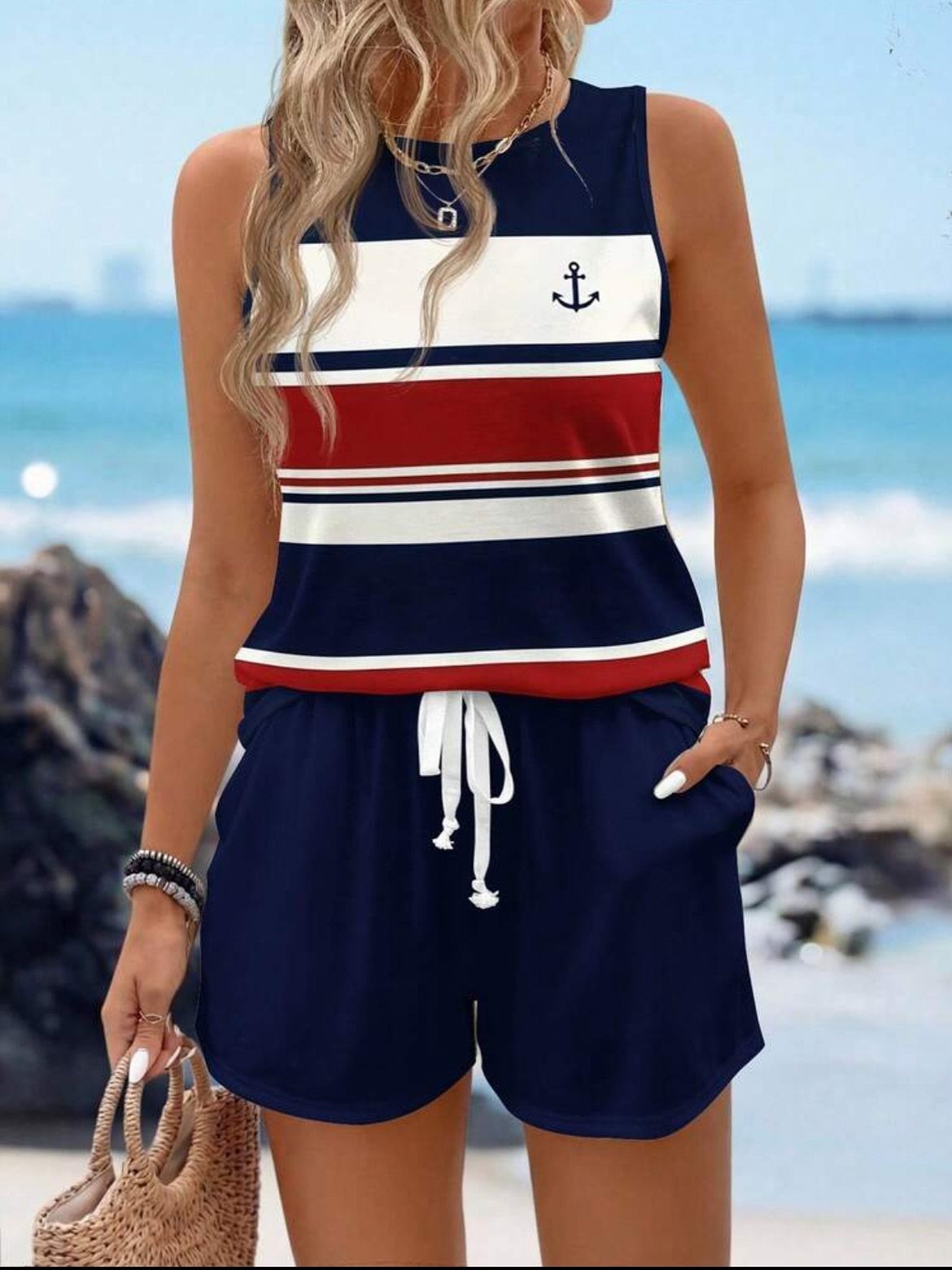 Woman wearing a striped navy, white, and red tank top and navy shorts on a beach.