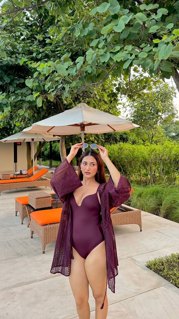 Woman in a purple swimsuit and lace cover-up posing on a sunny patio.