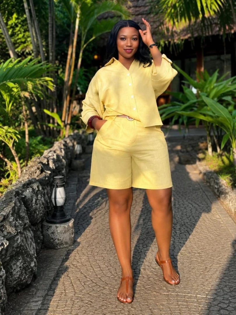 A woman posing in a yellow linen two-piece shirt and shorts set on a garden path.