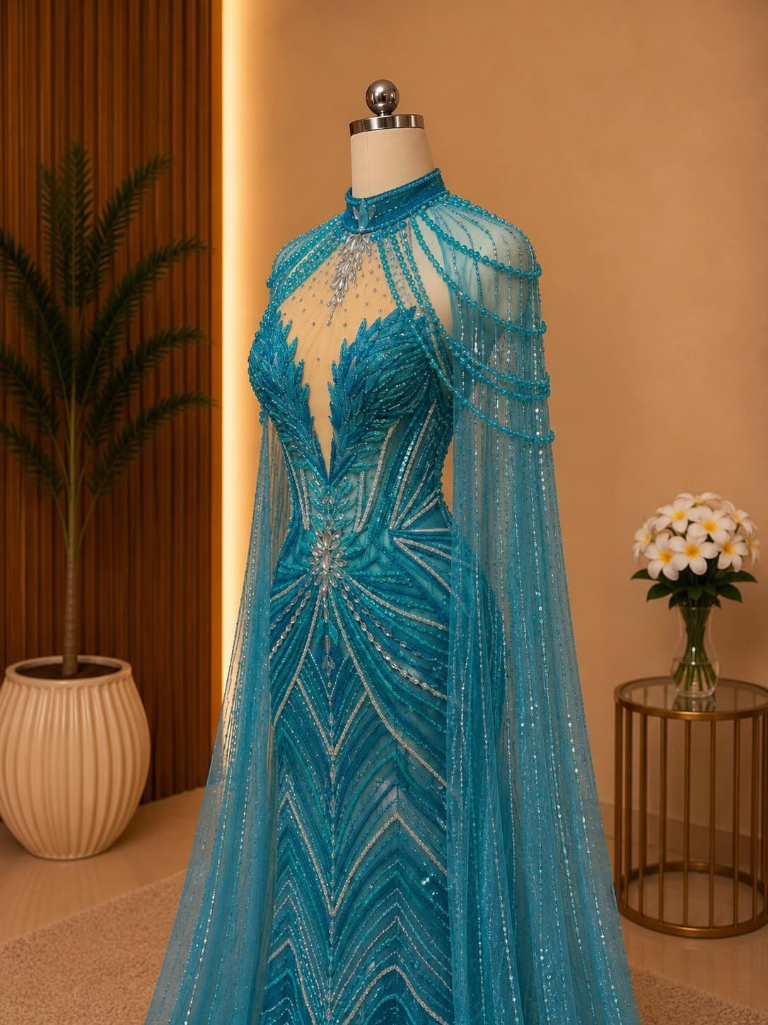 A teal beaded evening gown with a matching sheer cape displayed on a mannequin.