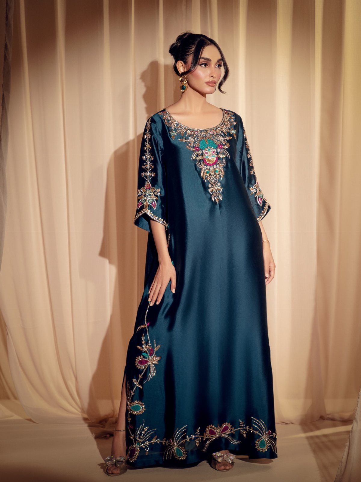 Woman in a teal beaded kaftan dress wearing green earrings and metallic heels.